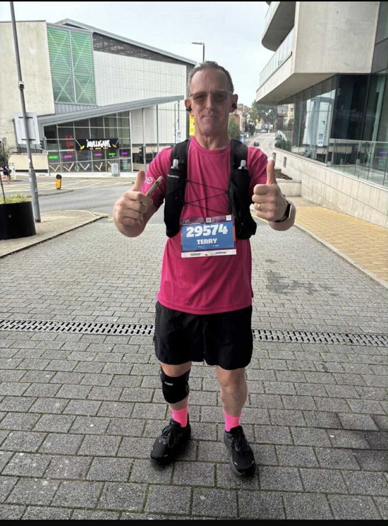 Man standing proud in a pink top having run a marathon