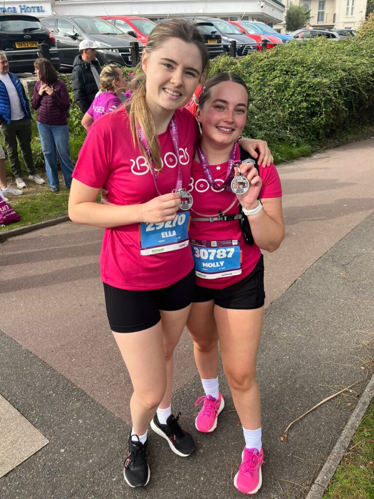 Two young girls standing with their marathon medals. Wearing pink tops.